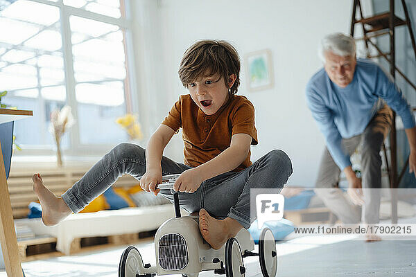Glücklicher Junge auf Spielzeugauto  der zu Hause mit Großvater spielt