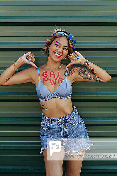 Lächelnde Frau mit Girl-Power-Text auf der Brust vor der Wand