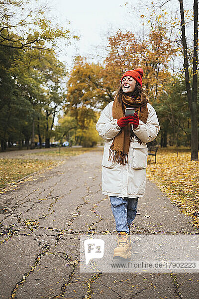 Glückliche junge Frau mit Smartphone läuft auf Fußweg im Park