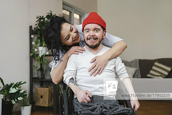 Smiling woman embracing boyfriend in wheelchair at home