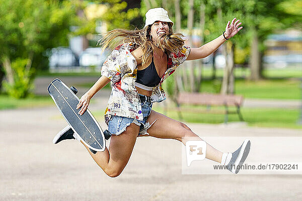 Carefree woman with skateboard jumping at park