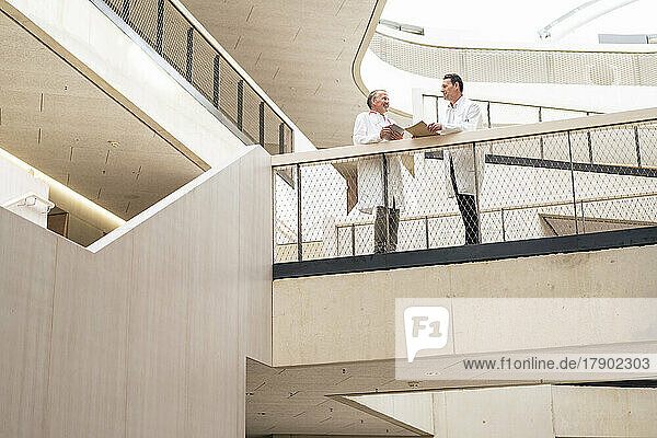 Lächelnde Mitarbeiter des Gesundheitswesens diskutieren miteinander und stehen neben dem Geländer im Krankenhausflur