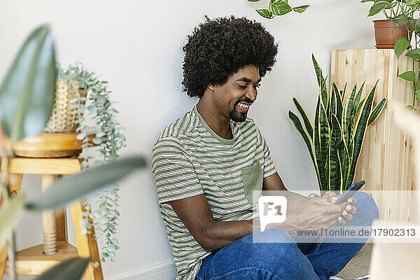 Happy man with Afro hairstyle using smart phone at home