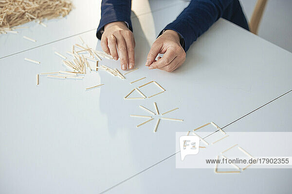 Hands of businesswoman making house model with sticks on table