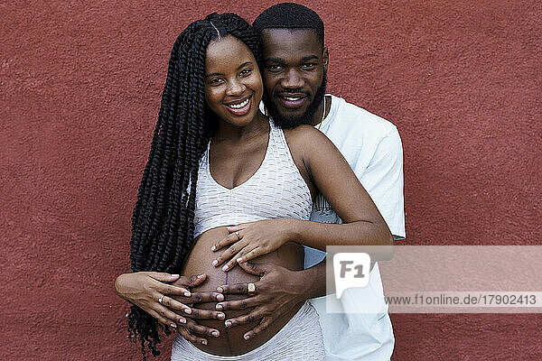Man embracing pregnant girlfriend in front of wall