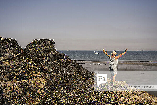 Senior woman with arms outstretched standing on rock at beach
