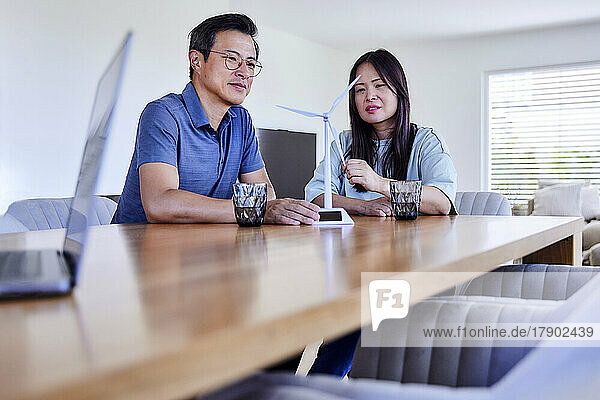 Smiling freelancers with wind turbine model sitting at table in living room