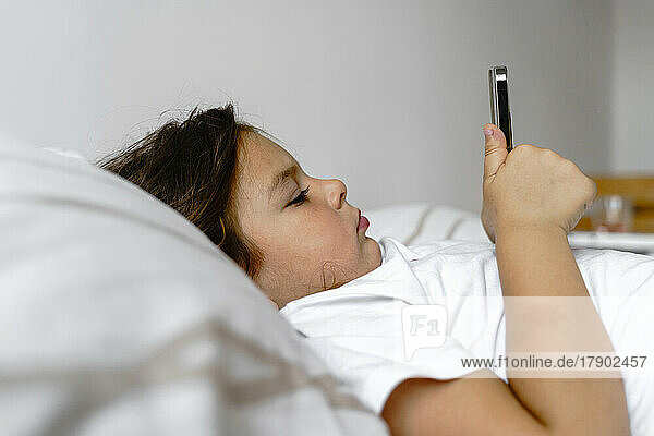 Mädchen benutzt Mobiltelefon und liegt zu Hause im Bett