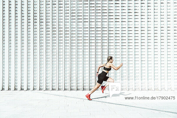 Young woman sprinting by white wall on sunny day