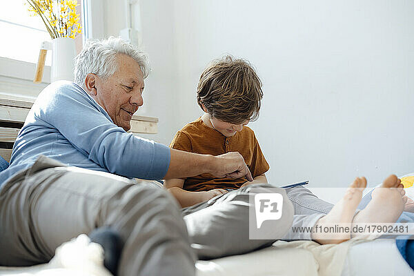 Smiling grandfather pointing at tablet PC by grandson in living room