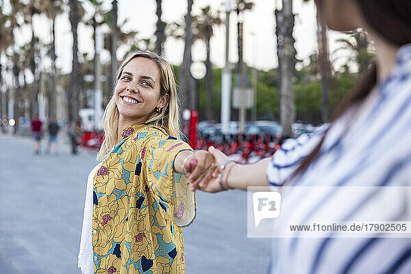 Smiling blond woman holding hand of friend at promenade