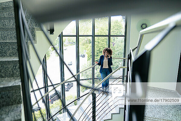 Businesswoman talking through mobile phone standing on staircase in office