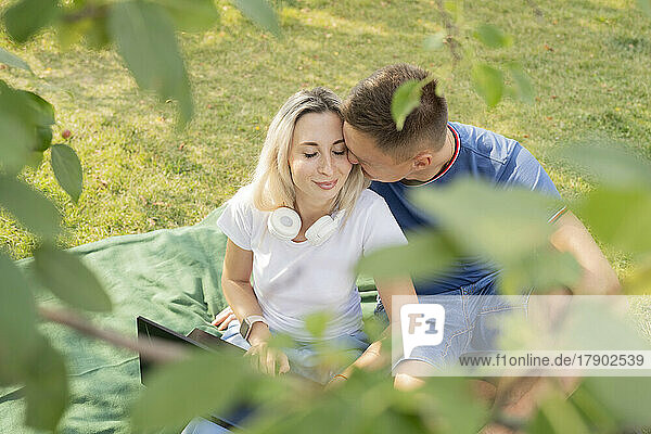Zärtlicher junger Mann küsst Freundin und genießt Picknick im Park