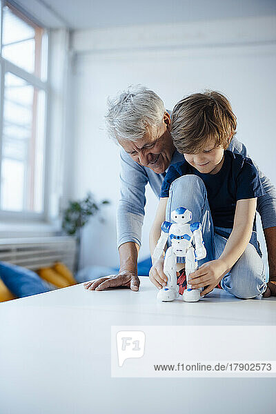 Boy playing with robot model by grandfather at home