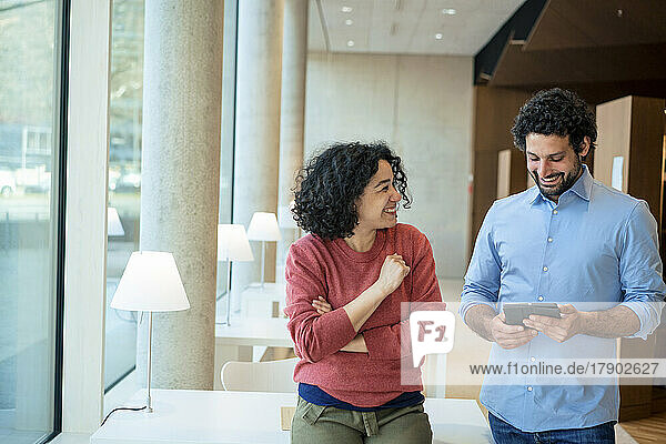 Happy man and woman discussing over tablet PC in library