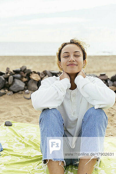 Smiling woman sitting with eyes closed enjoying at beach
