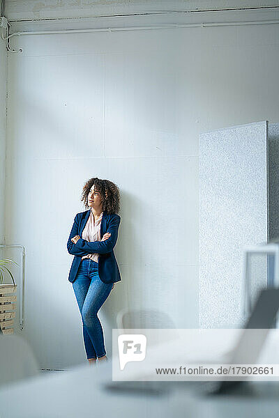 Thoughtful businesswoman with arms crossed leaning on wall