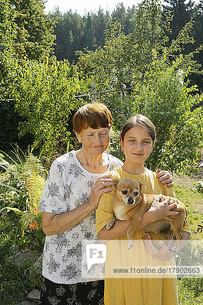 Großmutter und Enkelin stehen mit Hund im Garten