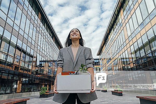 Glückliche Geschäftsfrau mit Karton vor Bürogebäude