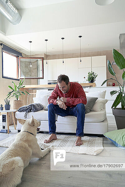 Mann sitzt zu Hause auf dem Sofa vor seinem Hund