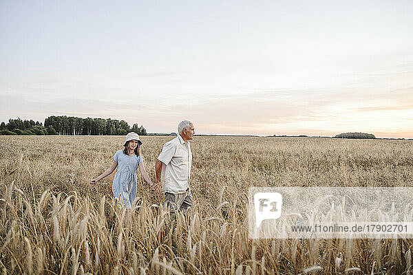 Senior farmer with girl walking in rye field