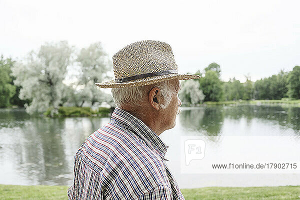 Senior man wearing hat by lake at park
