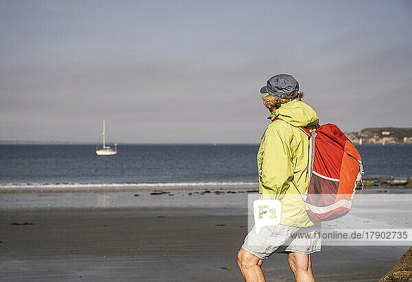 Senior woman with backpack standing at beach on sunny day