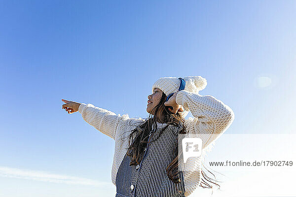 Girl enjoying music through headphones gesturing in front of blue sky