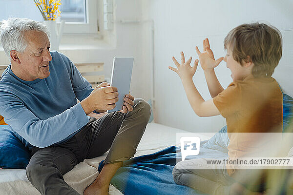 Älterer Mann fotografiert verspielten Enkel zu Hause über Tablet-PC