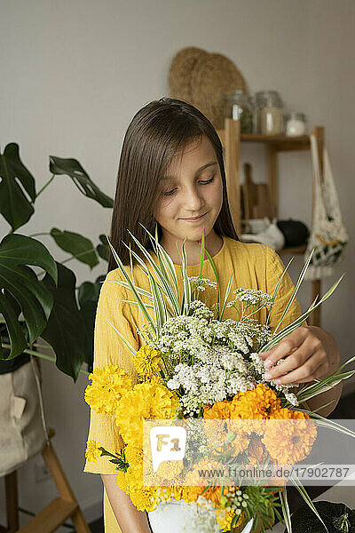 Smiling girl touching flowers in vase at home