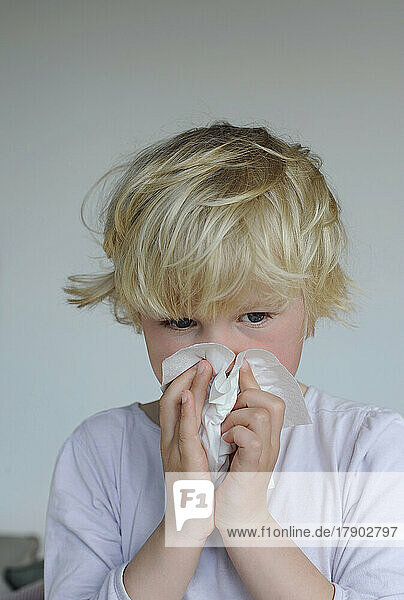 Ill girl with facial tissue cleaning nose at home