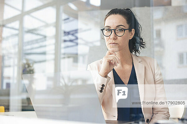 Confident businesswoman with laptop on table seen through glass