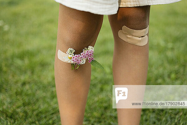 Girl with knees taped by bandage and flowers at park