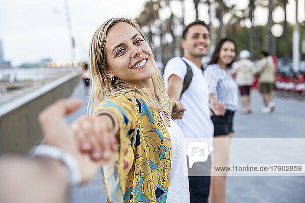 Smiling woman holding hands of friends enjoying at promenade