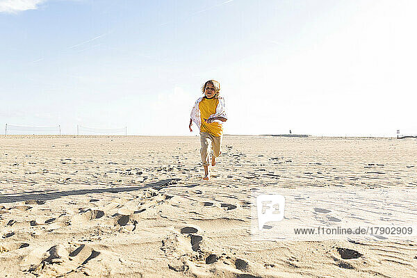 Playful boy running at beach on sunny day