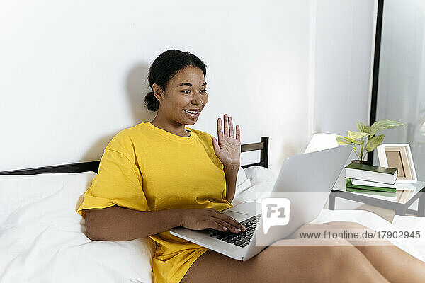 Frau sitzt im Bett und führt einen Videoanruf auf ihrem Laptop