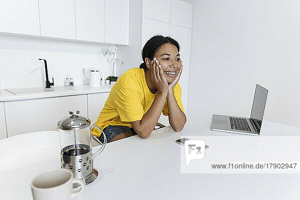 Happy freelancer sitting at the table in the kitchen with head in hands