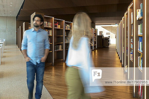 Blurred motion of man and woman walking in university library