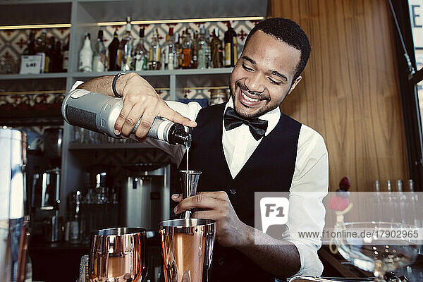 Smiling barman pouring syrup into jigger through bottle at bar