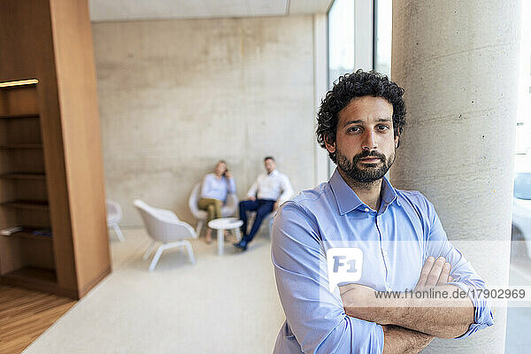 Confident professor with arms crossed leaning on column