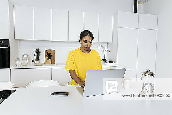 Junge Frau sitzt in der Küche und arbeitet am Laptop