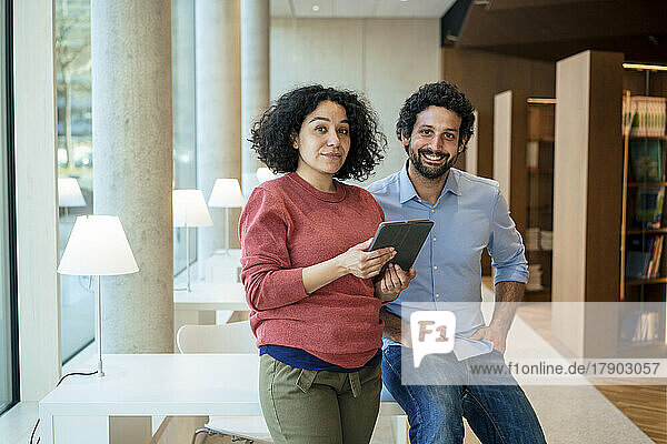 Smiling man and woman with tablet PC sitting on desk