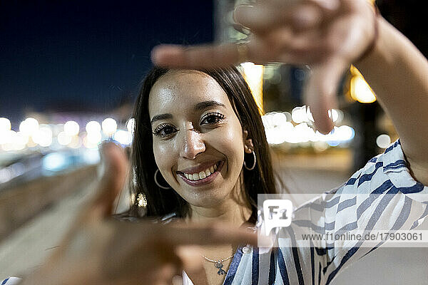 Happy young beautiful woman gesturing finger frame at night