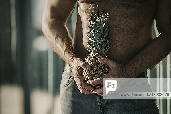 Shirtless mature man holding pineapple