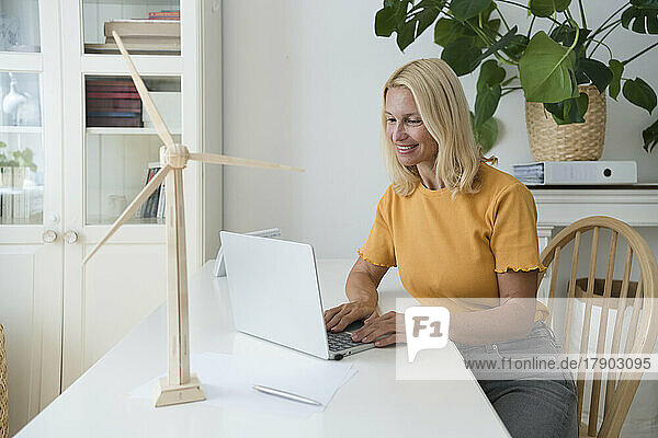 Lächelnder Freiberufler mit blonden Haaren  der am Laptop am Schreibtisch im Heimbüro arbeitet