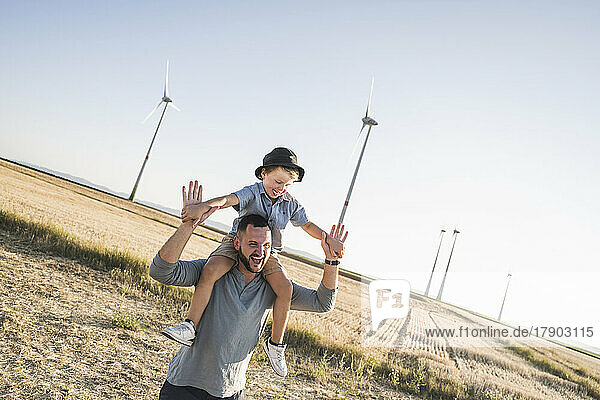 Father carrying son on shoulders in front of wind turbines