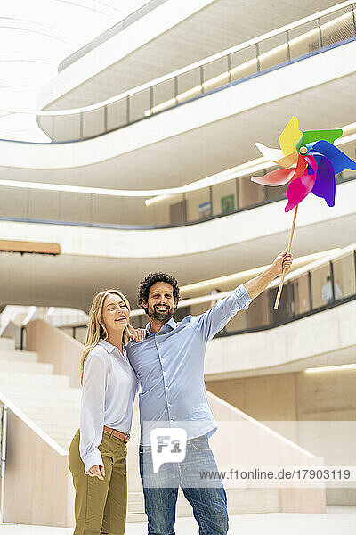 Smiling businesswoman with colleague holding multi colored pinwheel toy in office lobby