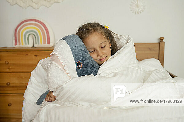 Girl sleeping with toy shark wrapped under white blanket in children's room