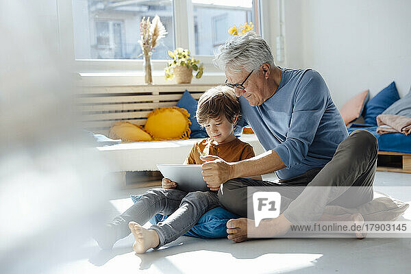 Älterer Mann nutzt Tablet-PC mit Enkel im Wohnzimmer