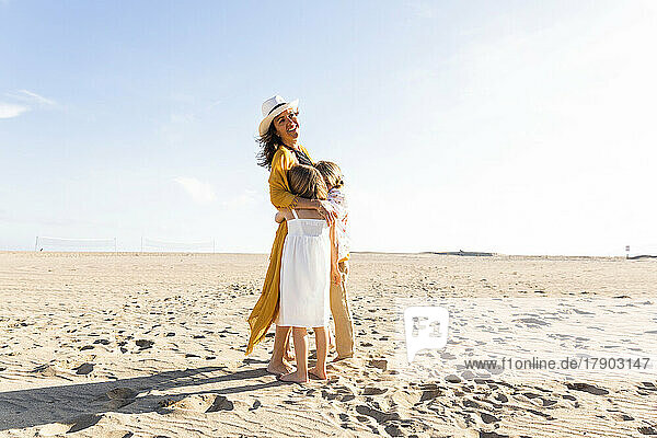 Happy mature woman hugging son and daughter at beach on sunny day